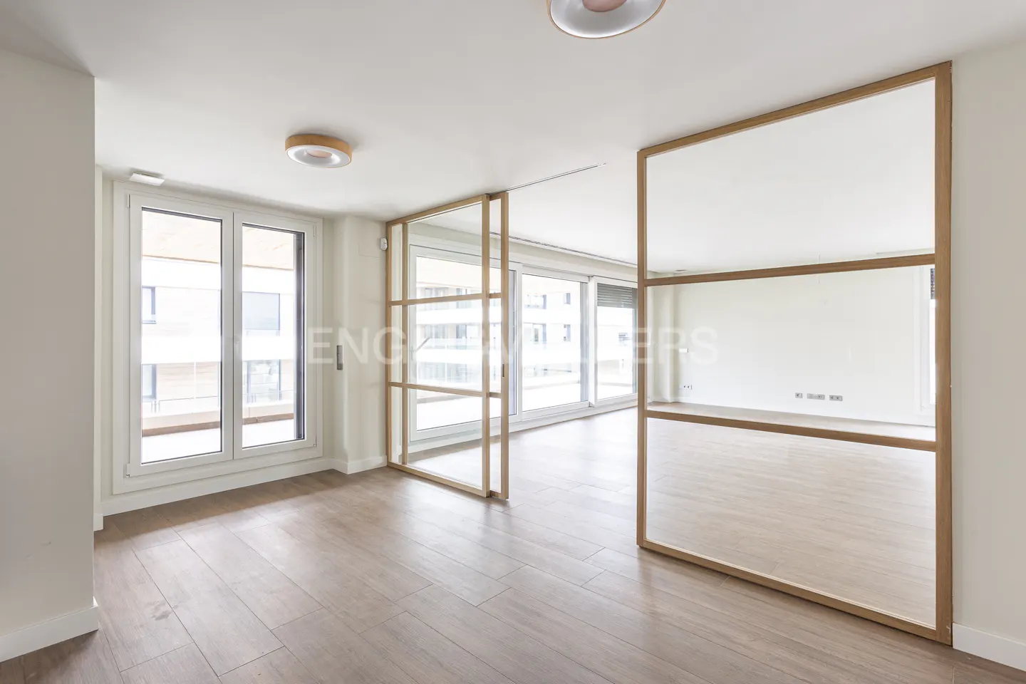Bright, modern room with light wood floors, white walls, and large windows separated by a wooden-framed glass partition.