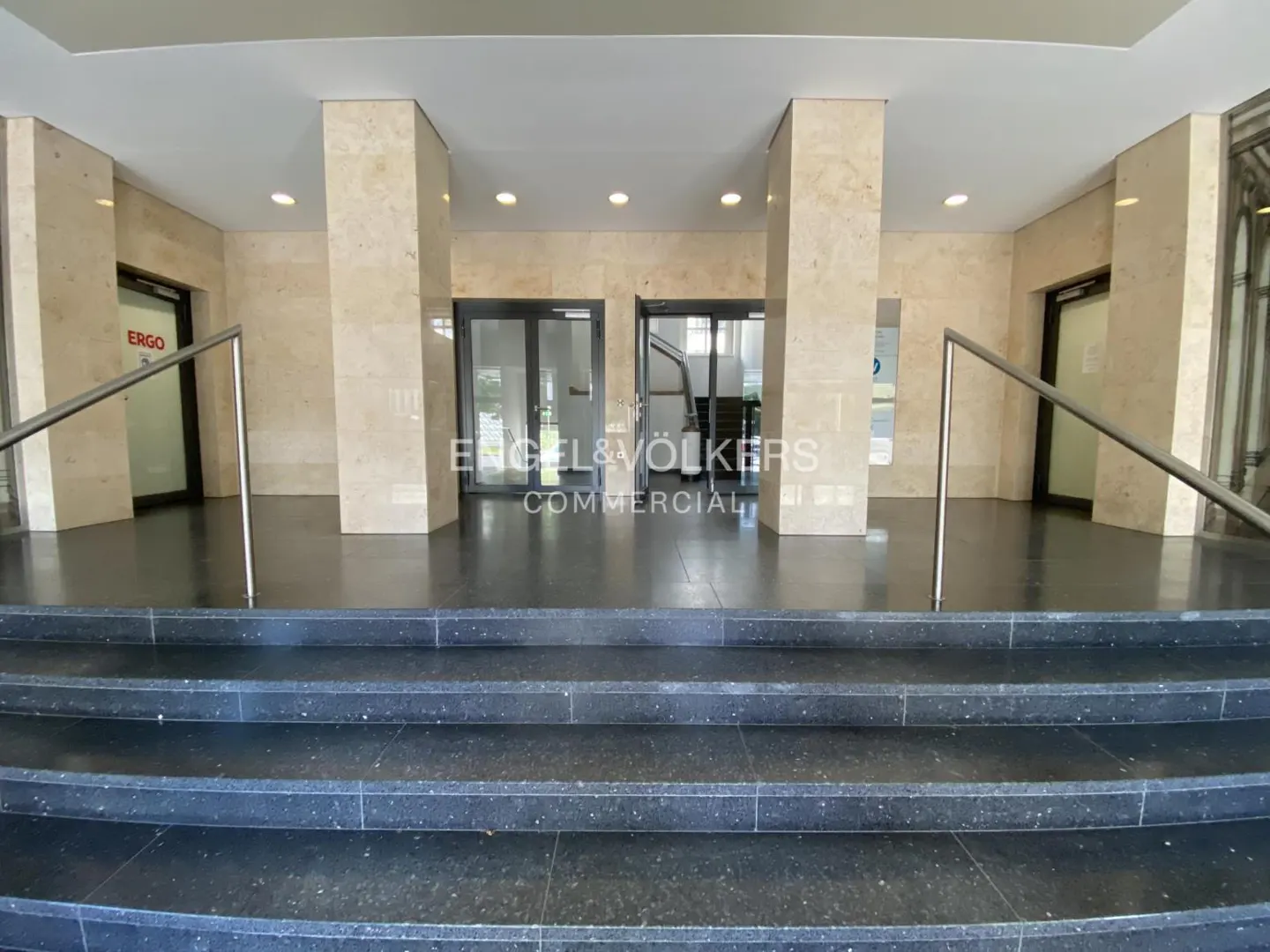 Commercial building entrance with black steps, marble pillars, and glass doors. Engel & Völkers Commercial logo visible.
