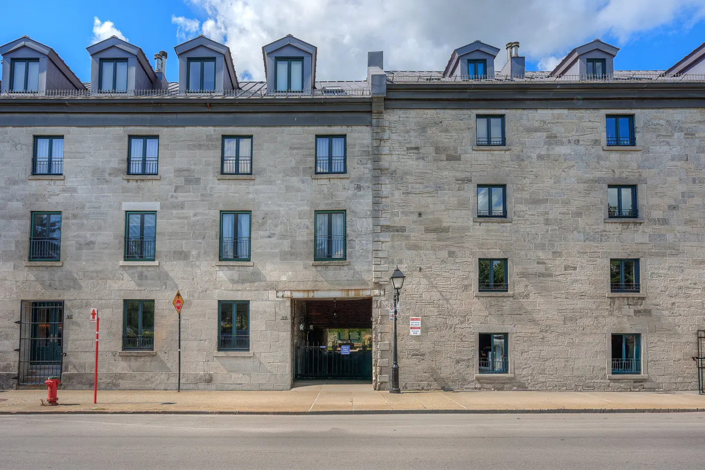 A four-story stone building with dark-framed windows and dormers under a partly cloudy sky.