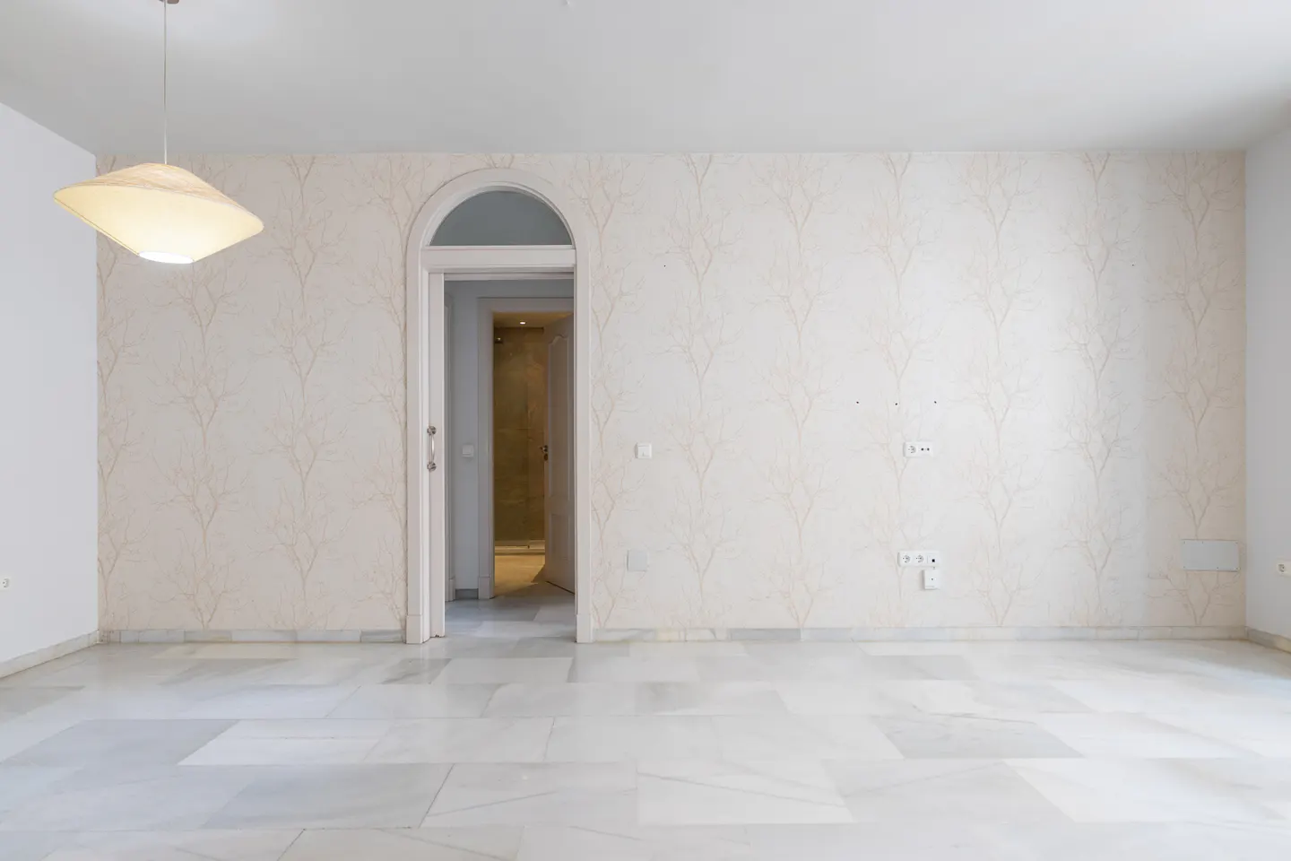 Empty room with marble floors, patterned wallpaper, and an arched doorway. A modern lamp hangs from the ceiling.