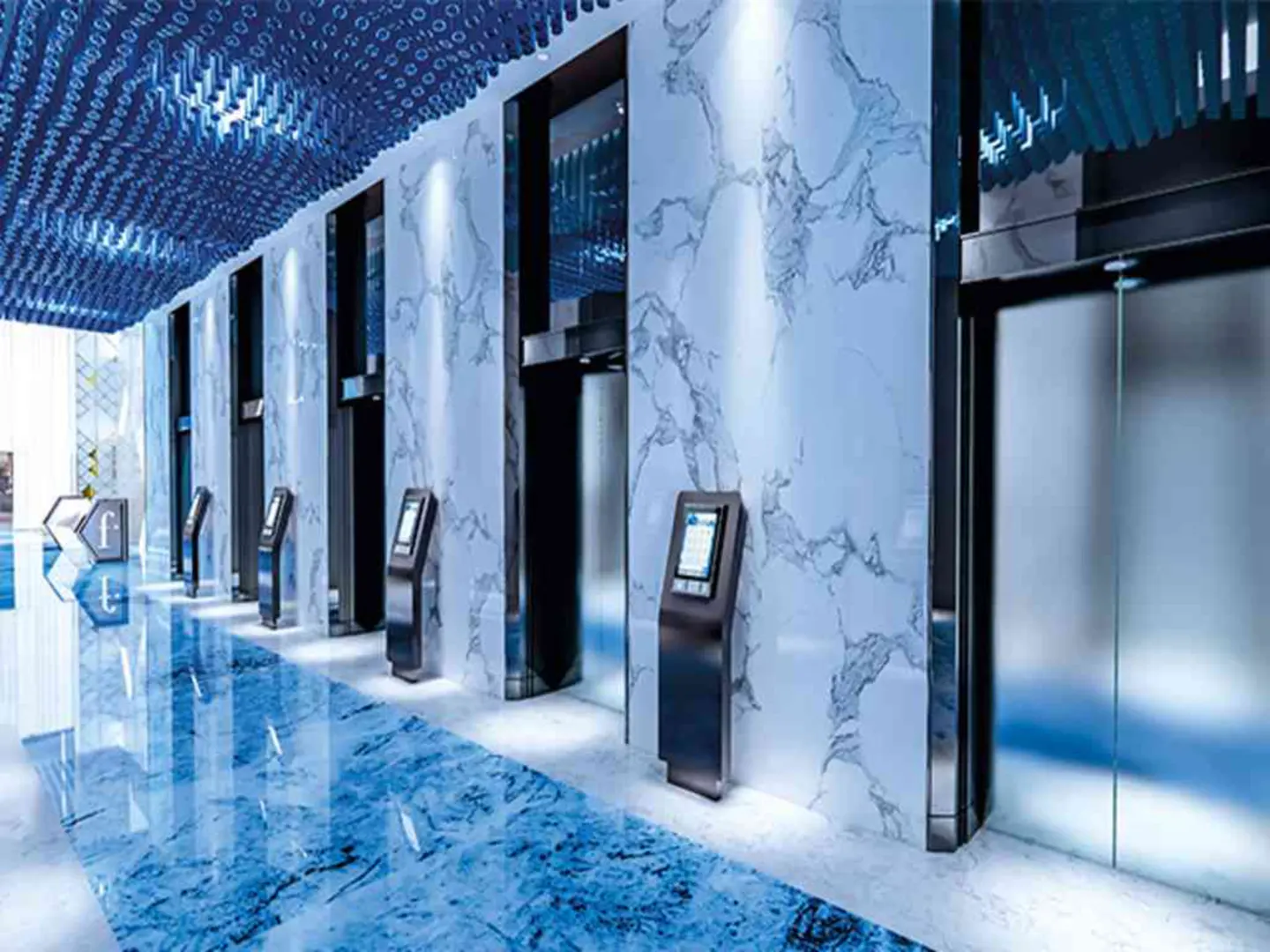 Modern elevator lobby with white marble walls, blue marble floors, and a decorative blue ceiling with touch-screen kiosks.