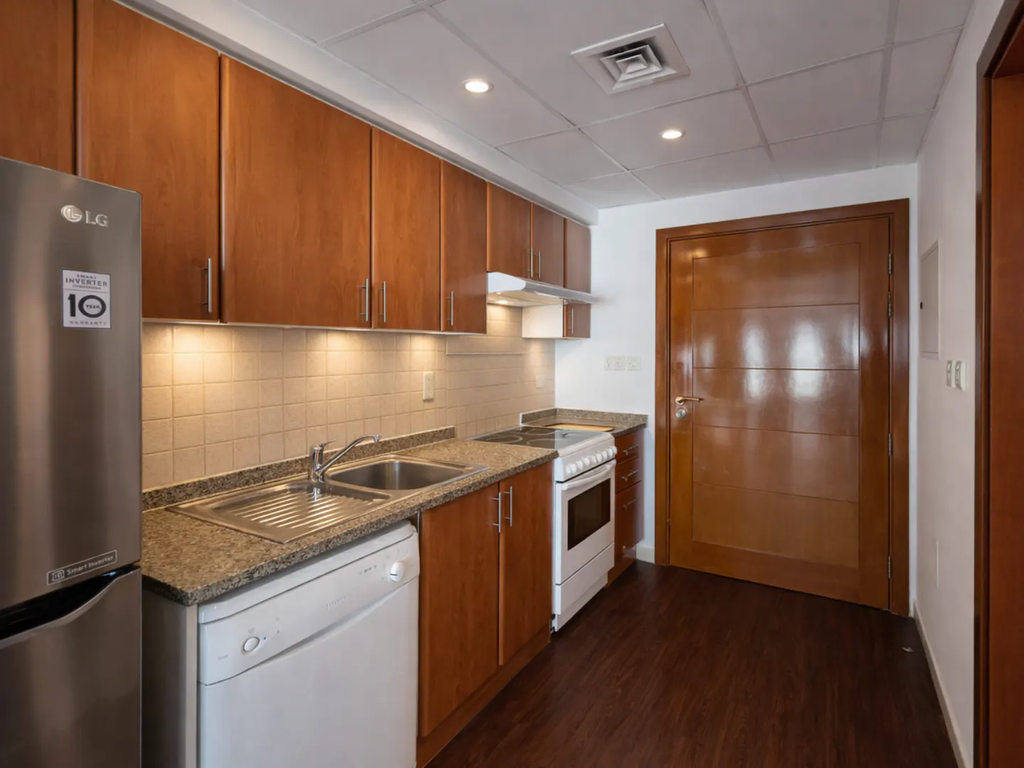 Kitchen with wood cabinets, granite countertops, stainless steel fridge, white dishwasher, and stove on dark wood floors.