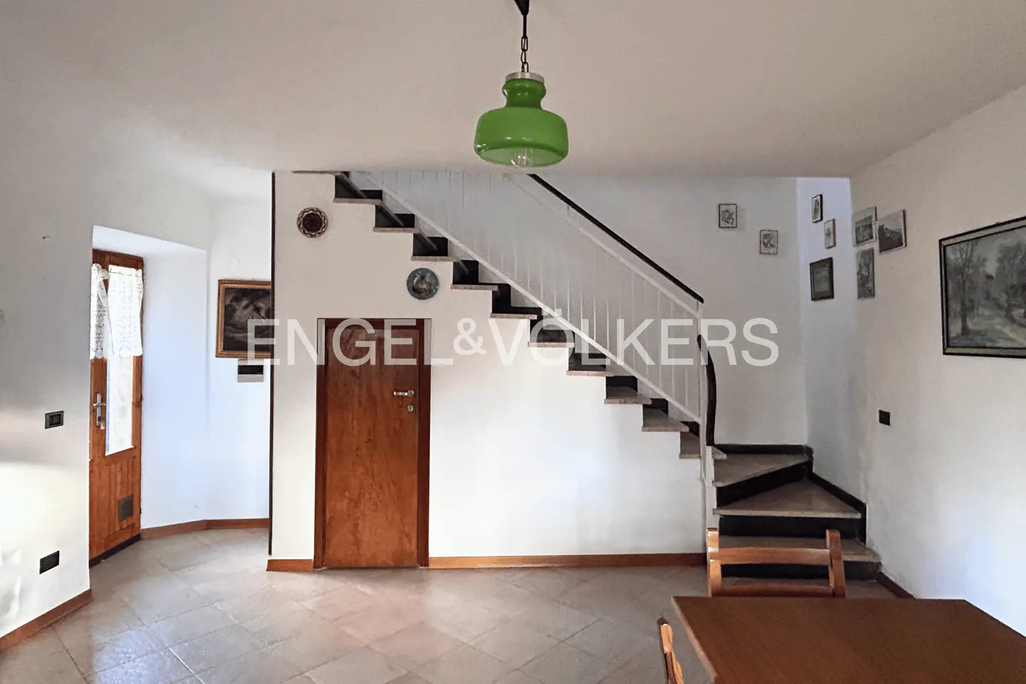 Interior view featuring a staircase with white railings, a wooden door, tiled floors, and a green pendant light.