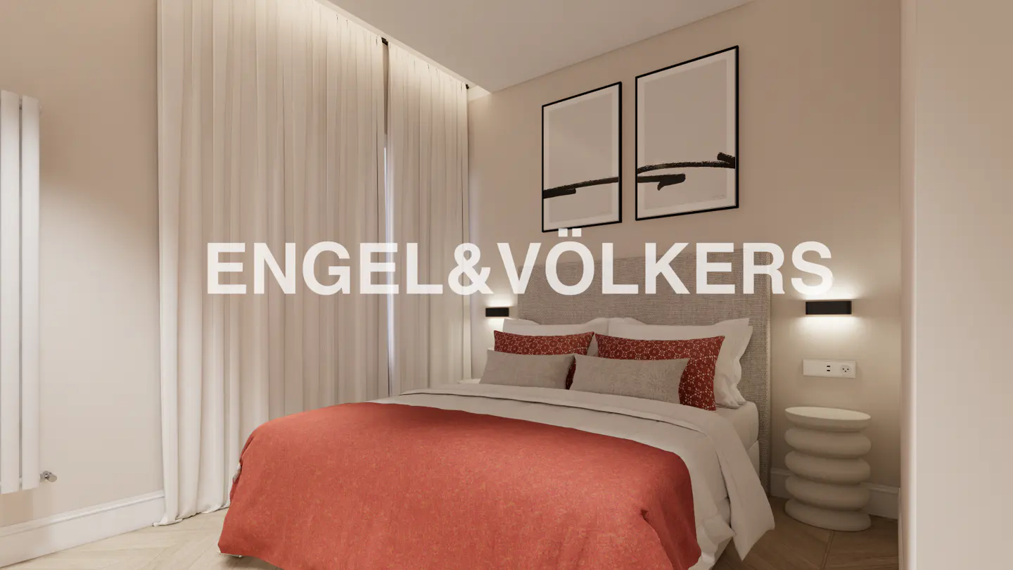 Bedroom with a bed covered in a red blanket, two framed pictures on the wall, and a white side table.
