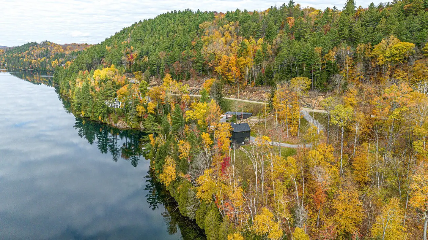 Aerial view of a lake house surrounded by colorful fall foliage and evergreen trees.