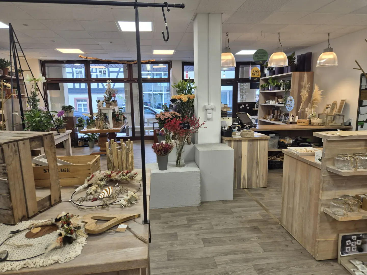 Interior view of a flower shop with wooden displays, flowers, and hanging lights.