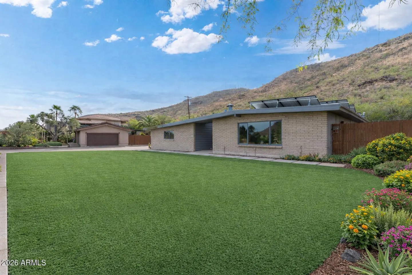 A tan brick house with a green lawn and a mountain in the background on a sunny day.