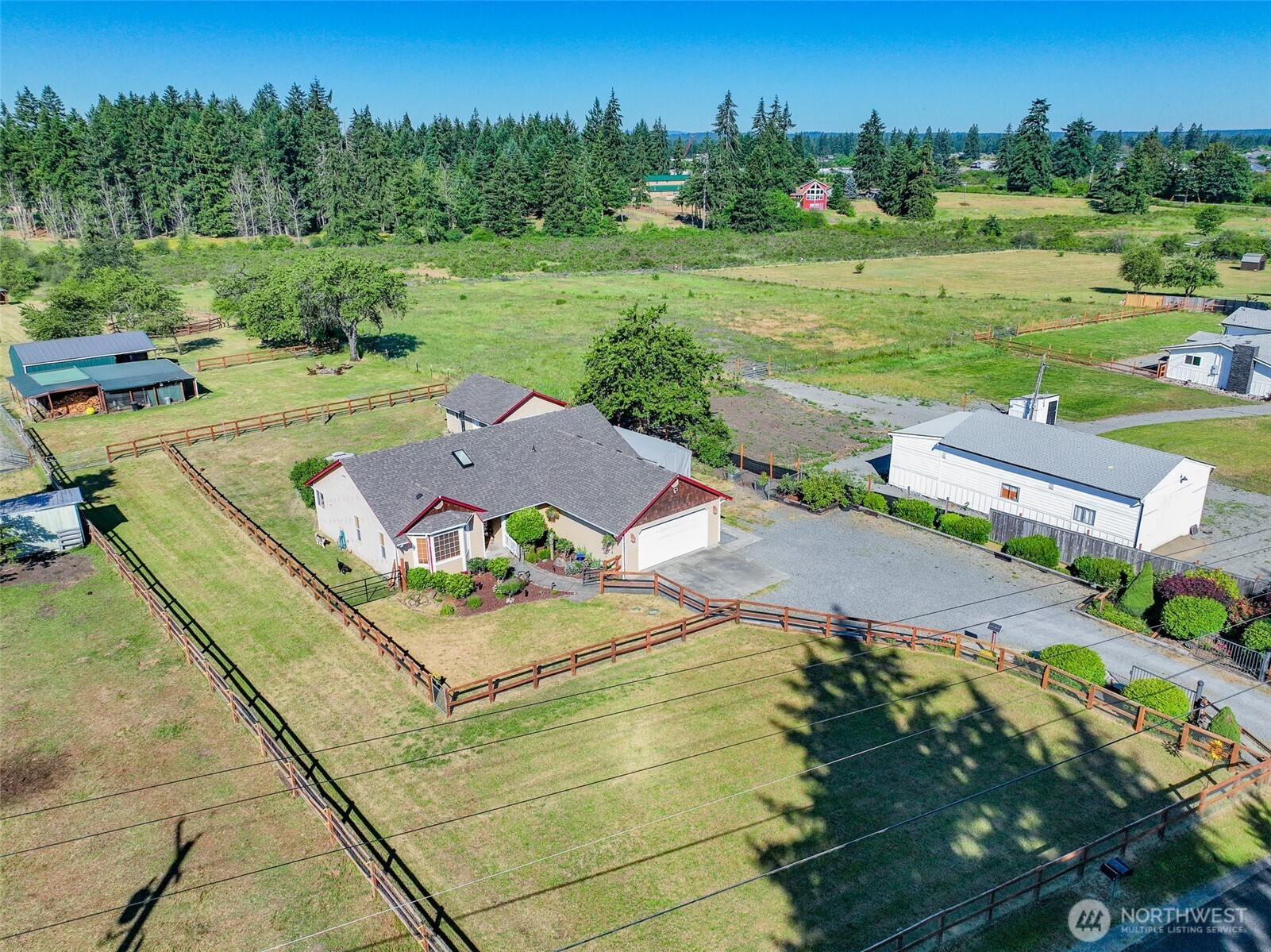 Aerial view of a ranch-style home with a large yard, fenced pastures, and a detached white workshop on a rural property.