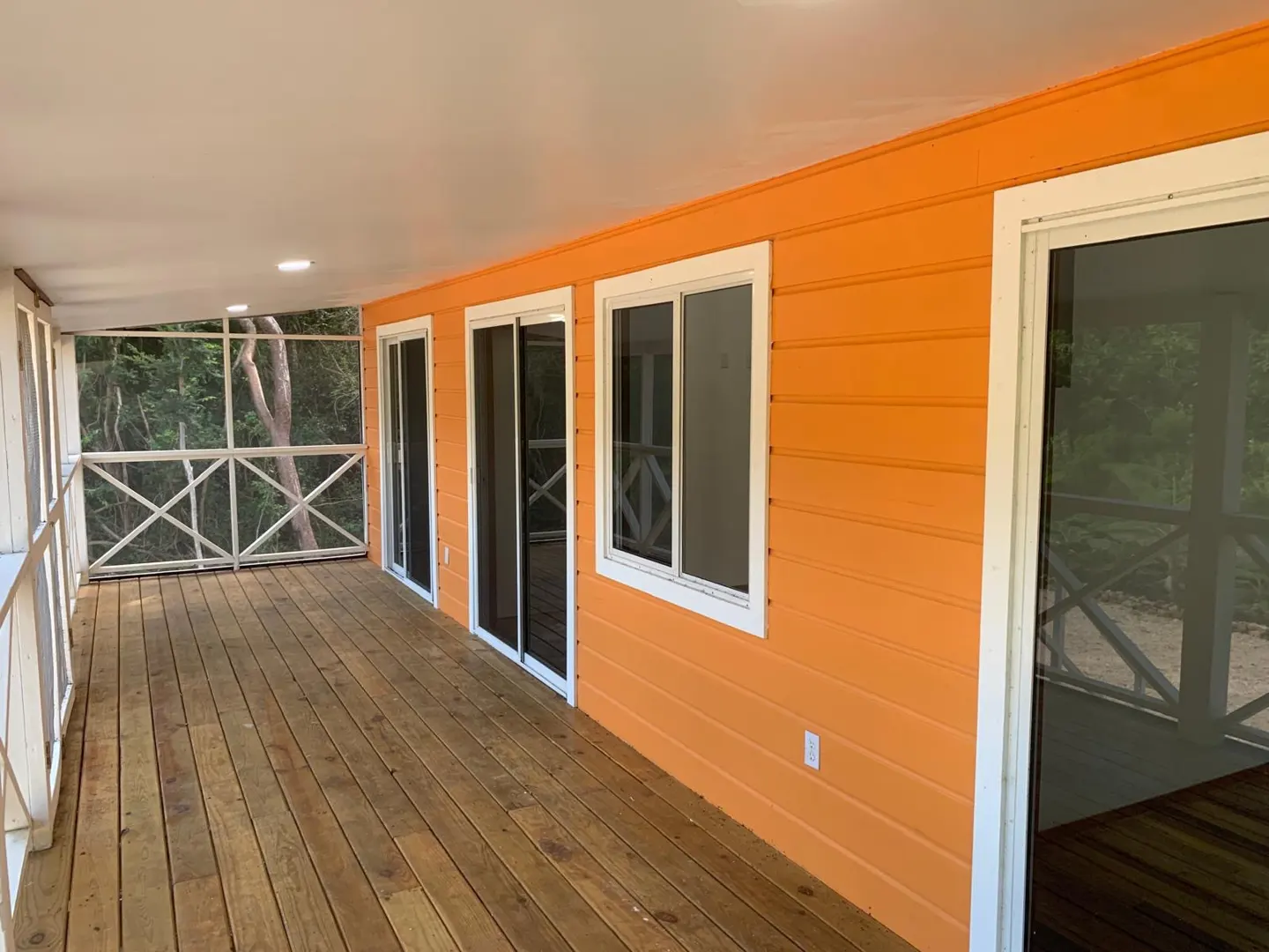Outdoor porch with wood floor, orange siding, white trim, screened railing, and sliding glass doors.