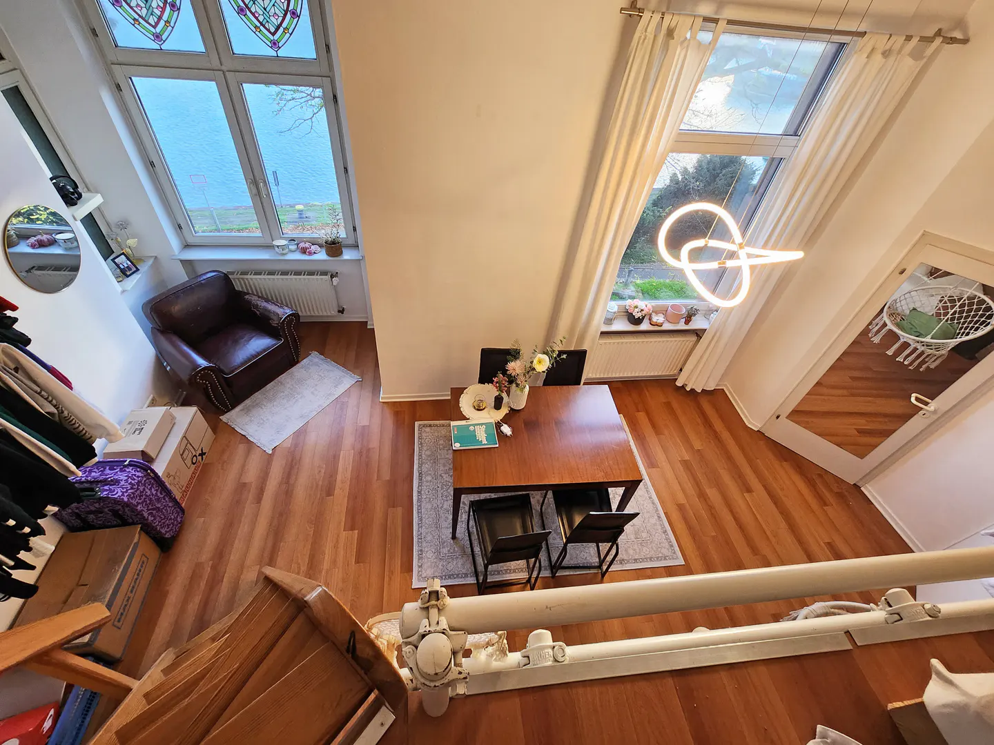 High-angle view of a dining area with a wooden table, four black chairs, a leather armchair, and large windows with views.