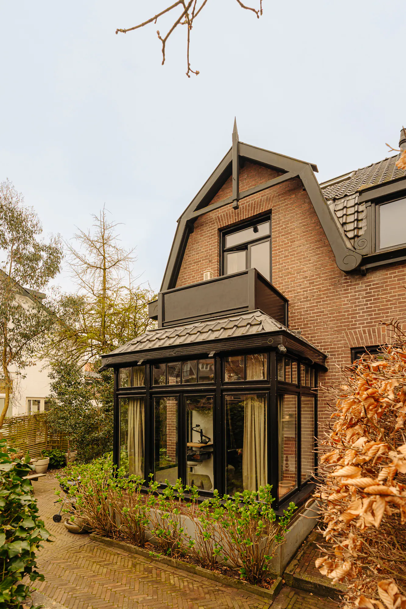 Exterior view of a brick house with a sunroom addition, black trim, and a brick walkway.