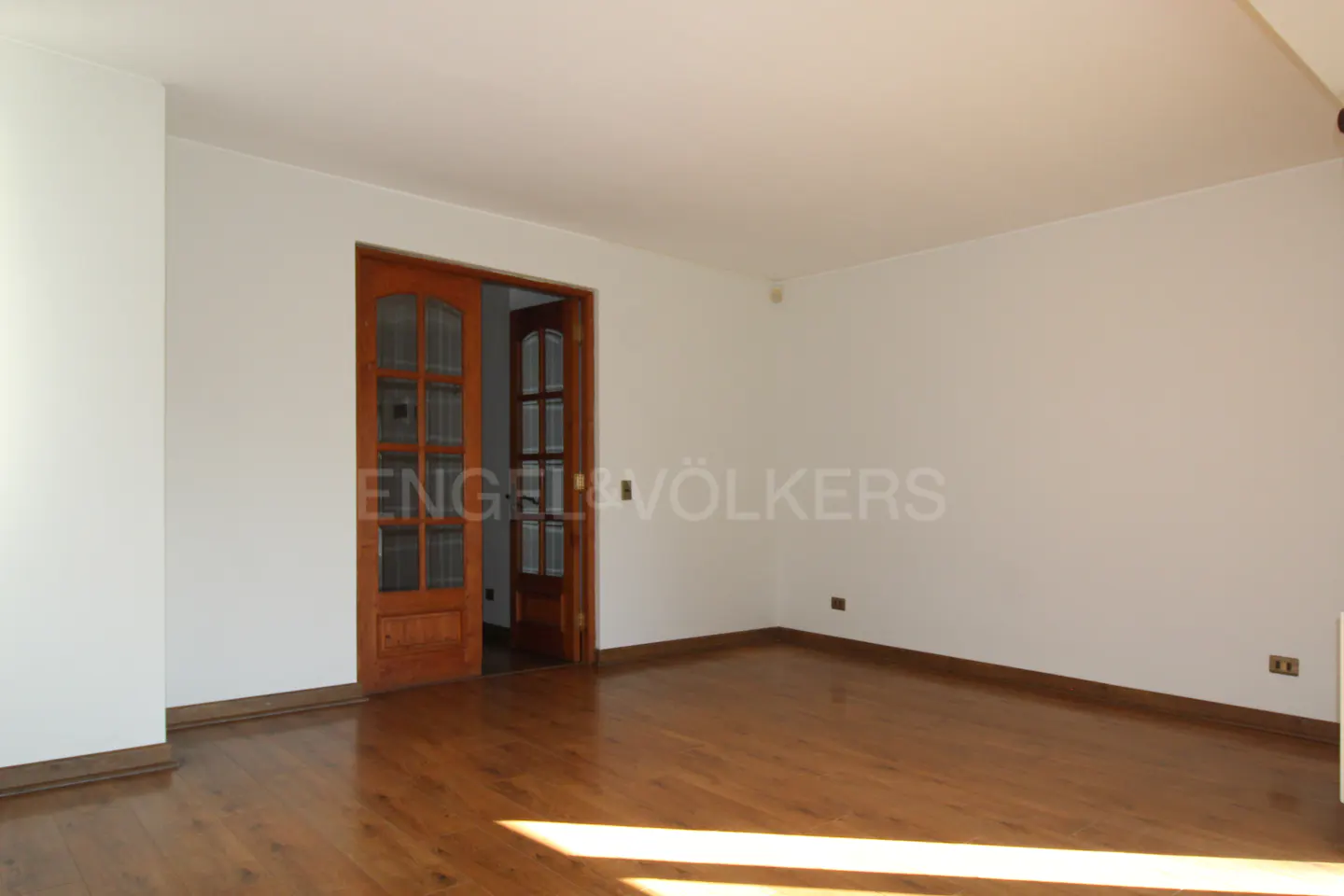 Empty room with wood floors, white walls, and an open wood-framed glass door. Engel & Völkers logo is visible.