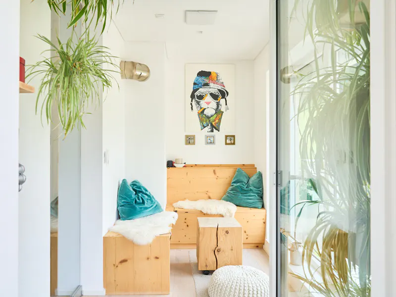 Bright, modern hallway with wooden bench, teal pillows, and a quirky cat portrait. Hanging plants add a touch of nature.