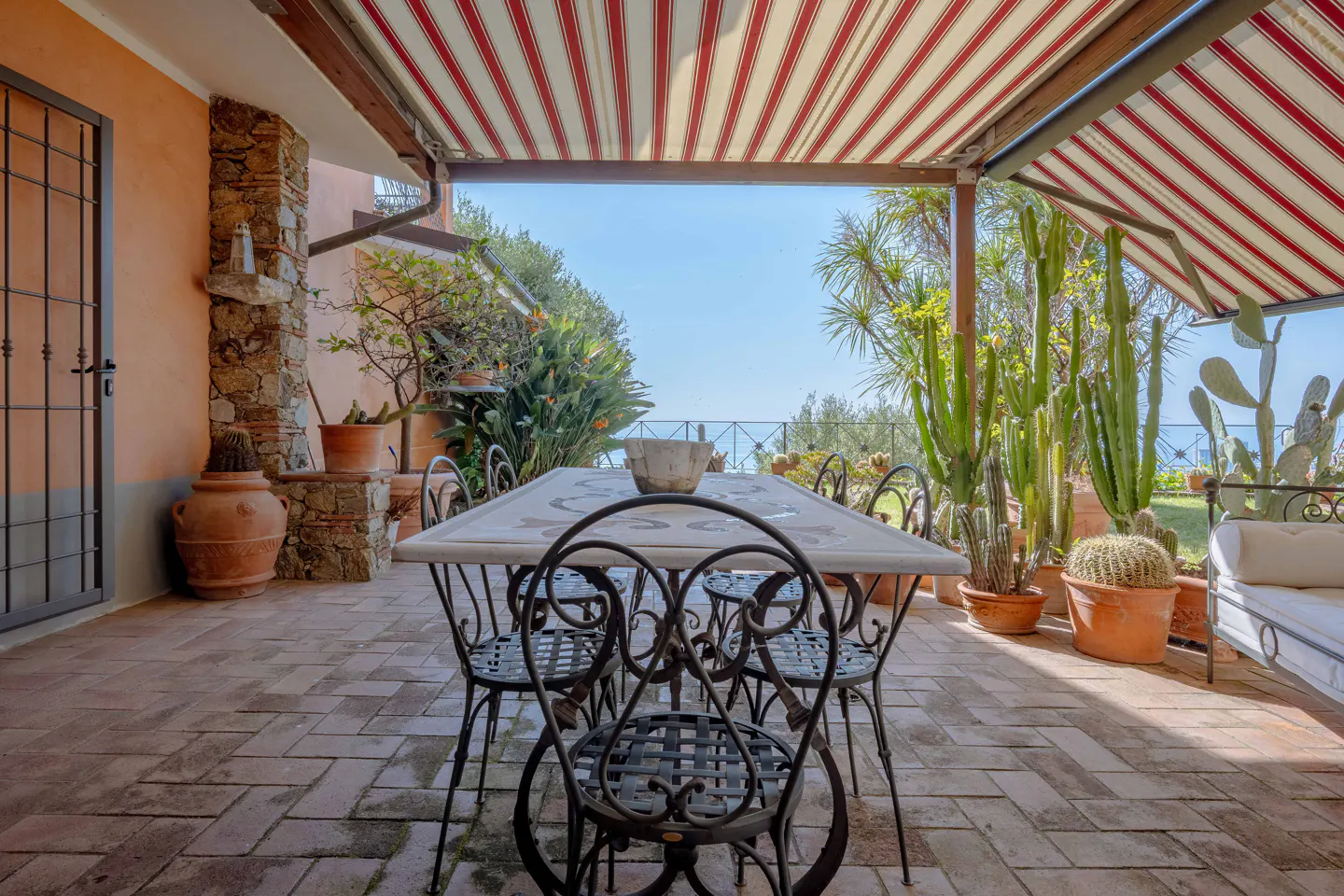 Outdoor patio with a table, chairs, and potted plants under a red and white striped awning.