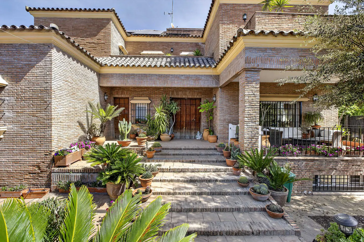Brick house with steps leading to a wooden door, potted plants lining the steps and porch.