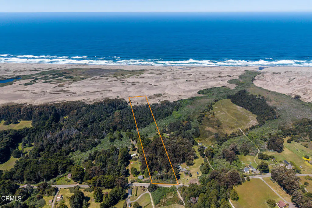 Aerial view of a property outlined in orange, near a beach and blue ocean. Trees and some houses are visible.