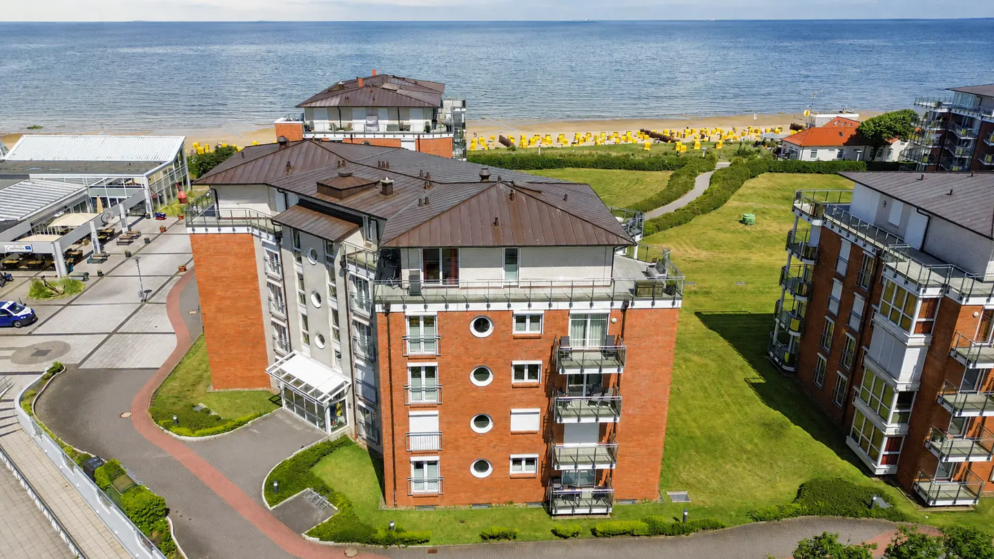 Aerial view of red brick apartment buildings with balconies near a sandy beach and the blue ocean.