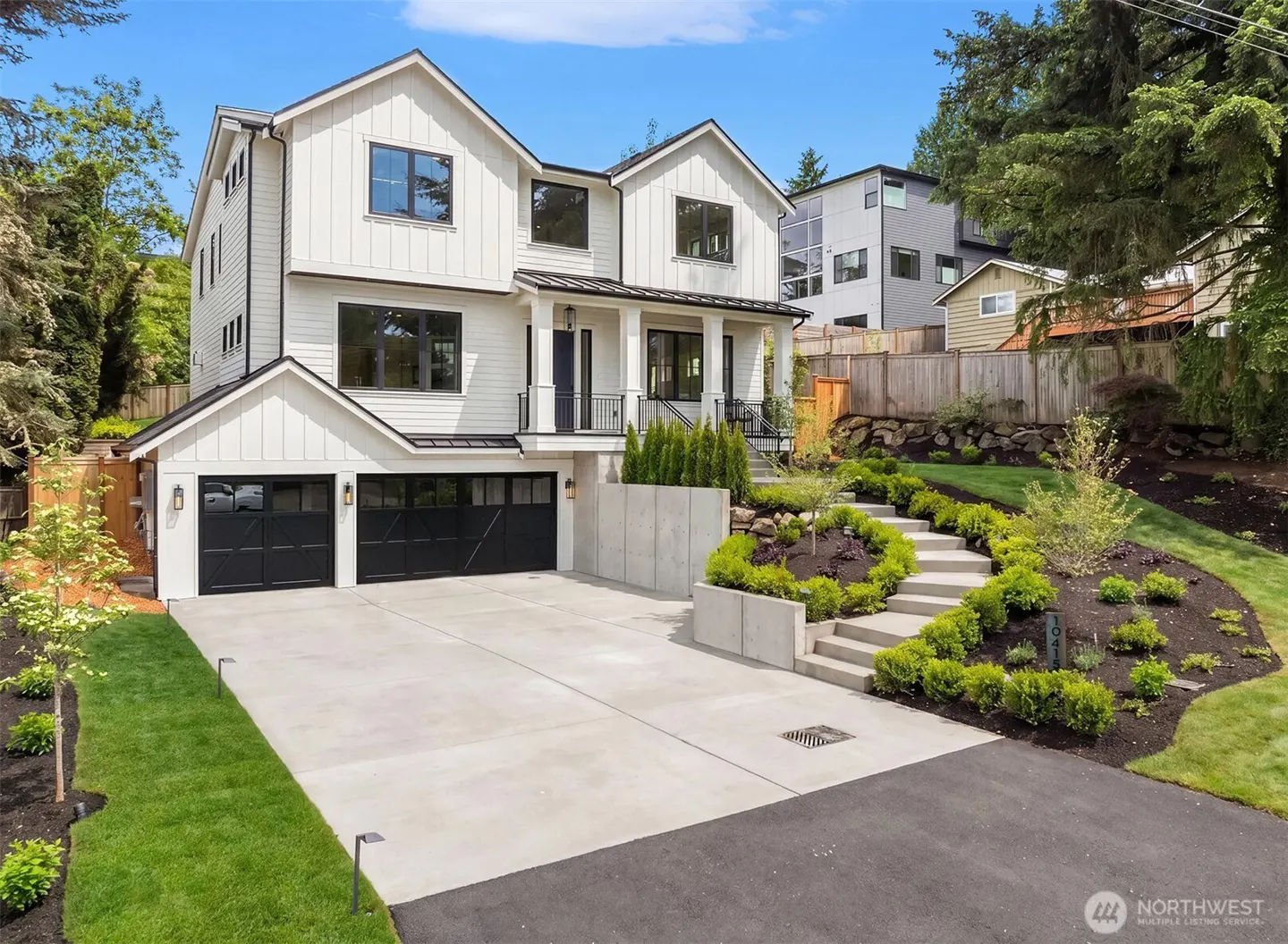 Modern white two-story house with black garage doors, concrete driveway, and landscaped stairs leading to the front door.