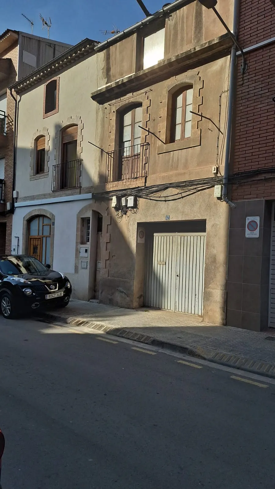 Two-story townhouses, one beige and one tan, with balconies and a black car parked in front.