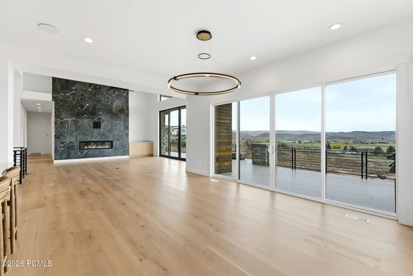 Bright, modern living room with light wood floors, a black marble fireplace, and large sliding glass doors to a balcony with a scenic view.