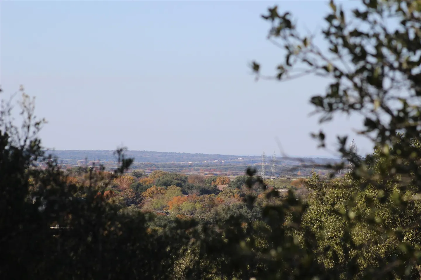 Scenic view of a distant landscape with trees in the foreground, under a clear blue sky.