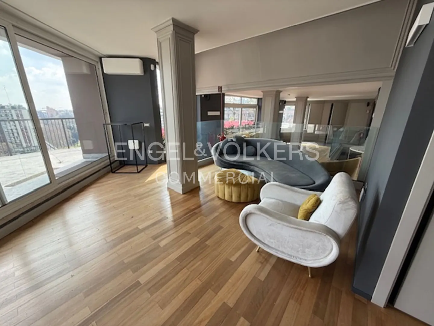 A bright, modern living room with hardwood floors, a white chair, and a large window overlooking a city.