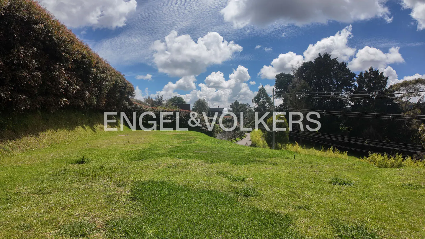 Lush green lot with Engel & Volkers logo, under a blue sky with puffy white clouds. Trees and power lines in the background.