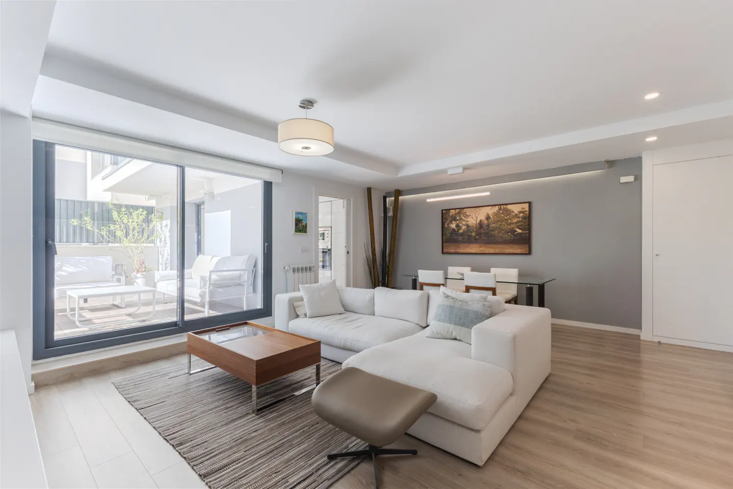 Bright living room with white sectional sofa, wood coffee table on a rug, and a patio view through sliding glass doors.