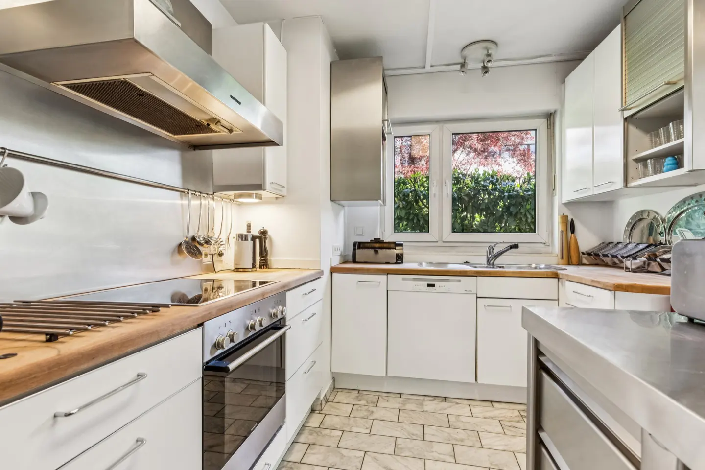 Modern kitchen with white cabinets, wooden countertops, stainless steel appliances, and a window overlooking greenery.