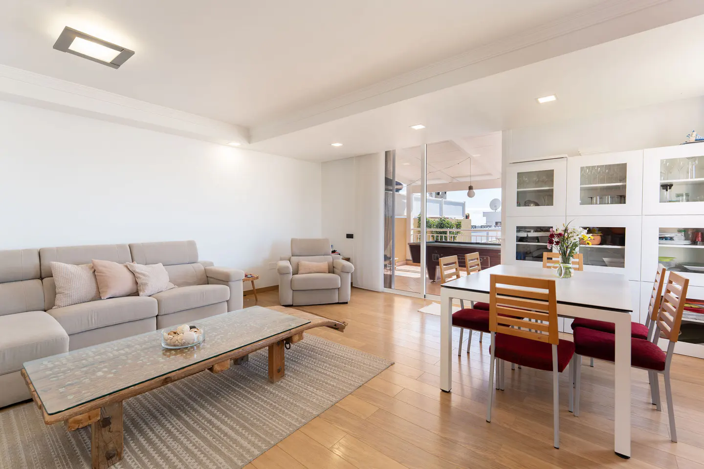 Bright living room with beige sofa, rustic glass coffee table, and white dining set near a balcony.