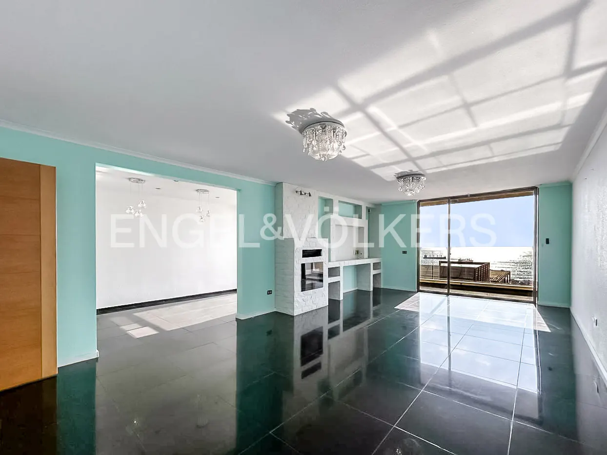 A bright, empty living room with black tile floors, a white fireplace, and a view of the ocean.