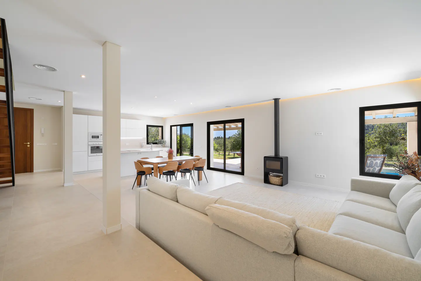 Bright, open-plan living space with white walls, a cream sofa, and a modern fireplace. A dining table and kitchen are visible in the background.