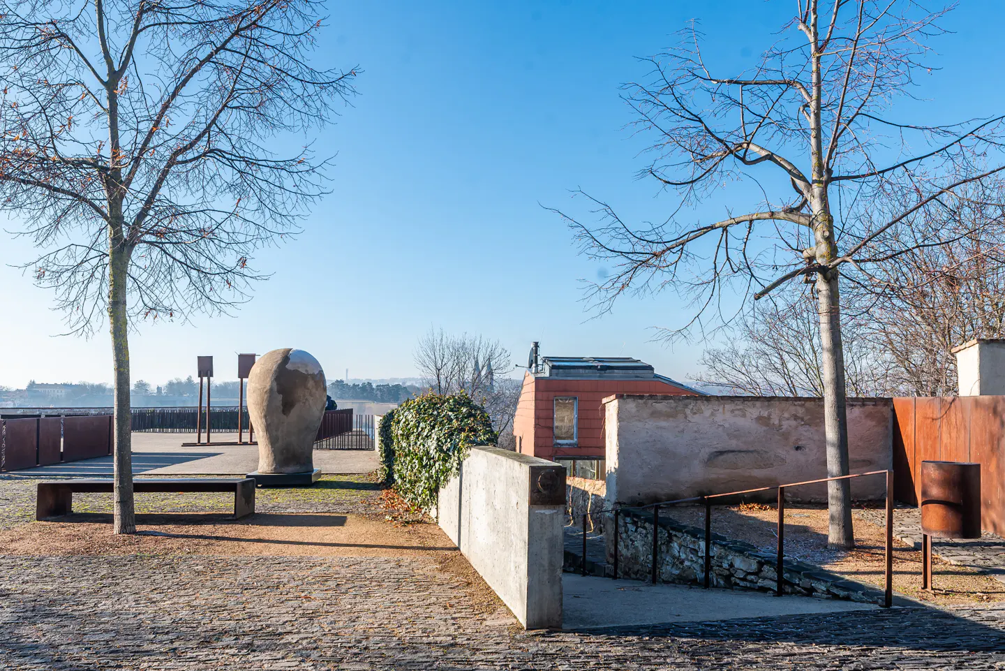 Outdoor view of a park with trees, a bench, and a large head sculpture on a sunny day.