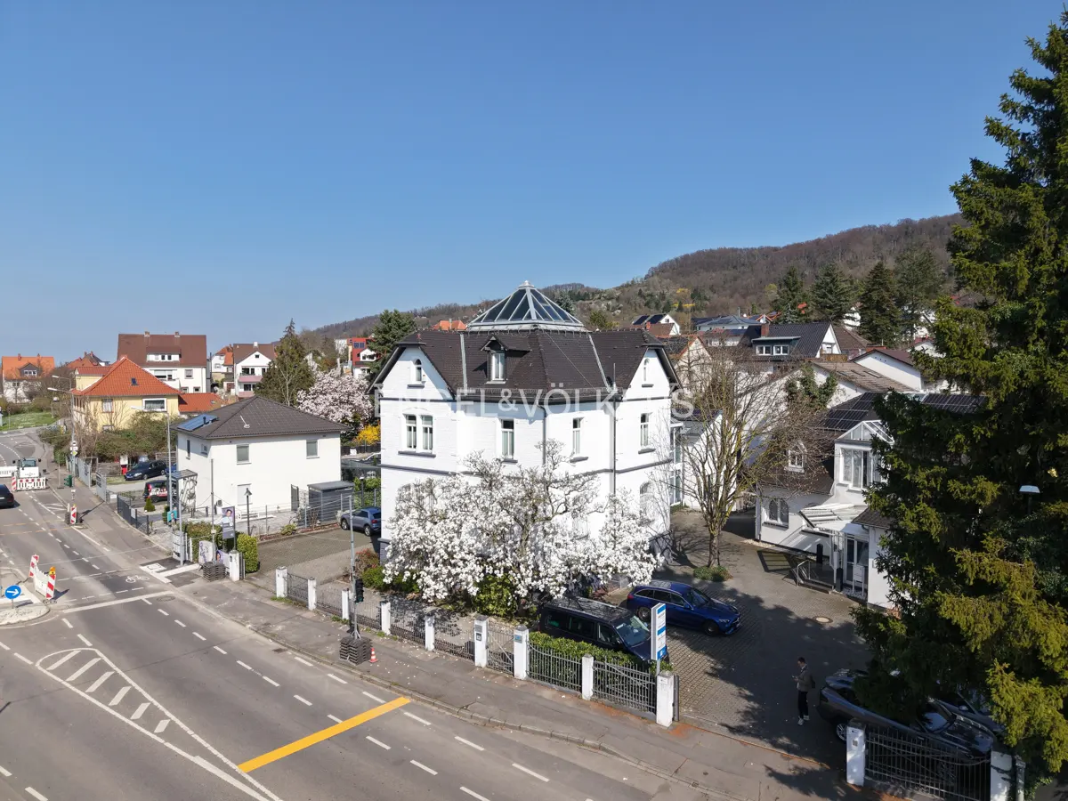 Engel & Völkers white building with a glass dome, surrounded by trees and cars, on a sunny day.