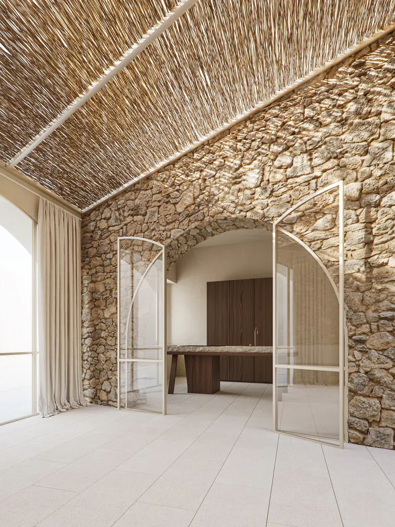 Interior view of a room with stone walls, a straw ceiling, and arched glass doors. A wooden table and cabinets are visible in the background.