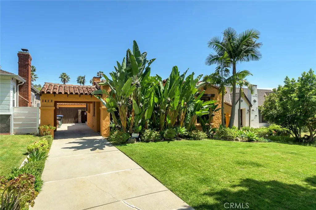 Exterior of a yellow house with a red tile roof, green lawn, and palm trees.