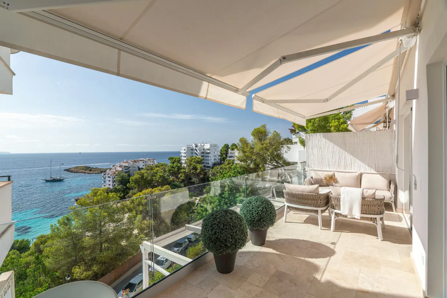Balcony view with beige awning, glass railing, and outdoor furniture overlooking the ocean and coastline.