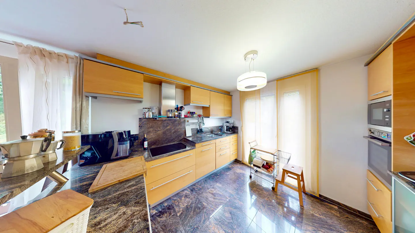Bright kitchen with light wood cabinets, marble countertops and floors, stainless steel appliances, and natural light from sheer curtains.