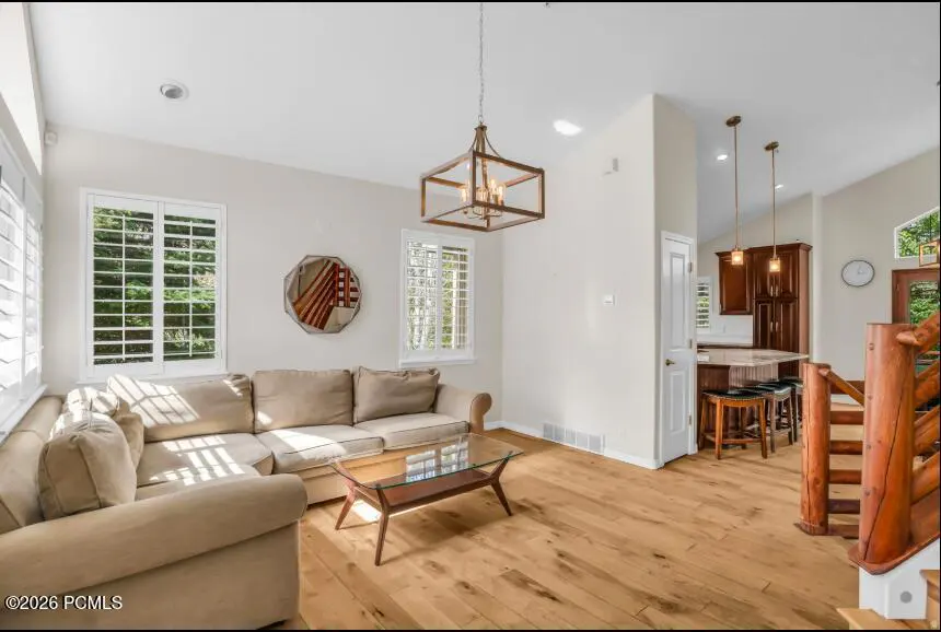 Living room with a beige sectional sofa, glass coffee table, wood floors, and a view into the kitchen.