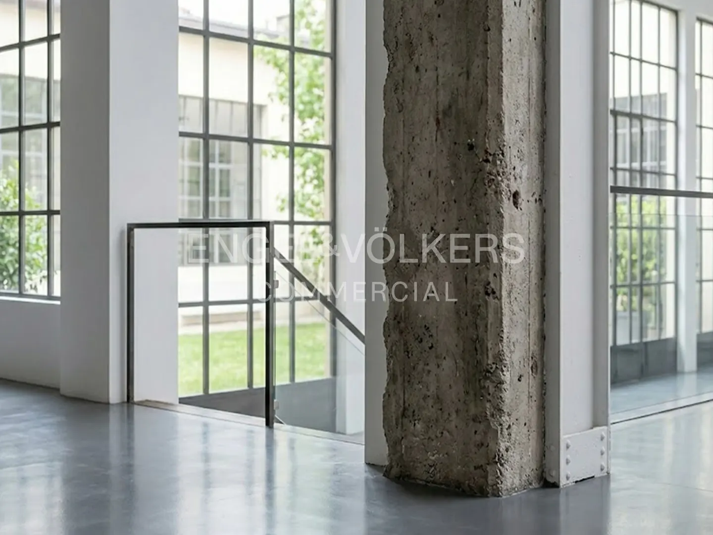 Interior view of a modern commercial space with a concrete pillar, large windows, and a staircase.