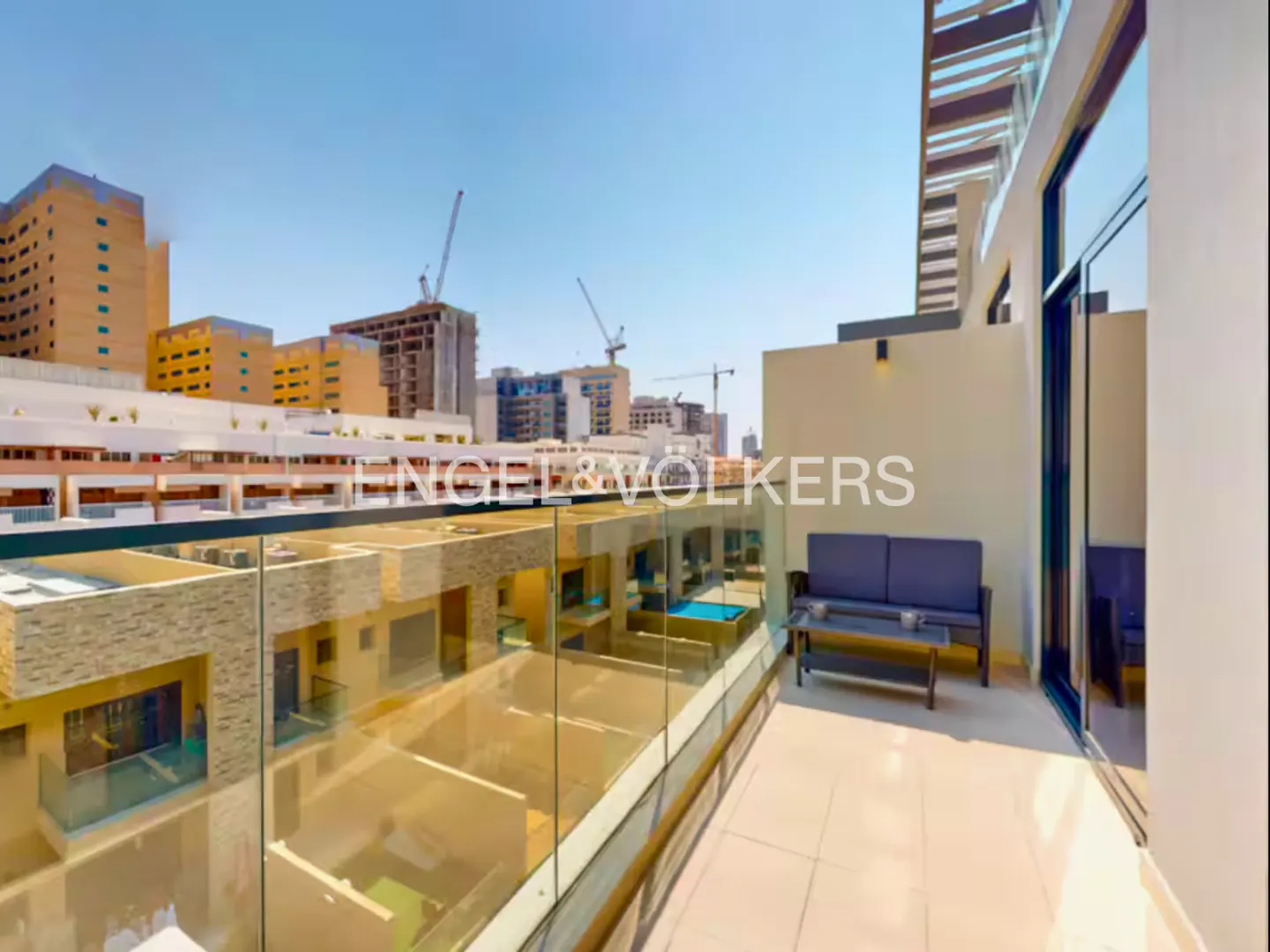 Balcony view with glass railing, outdoor seating, and city skyline. Engel & Volkers logo visible.
