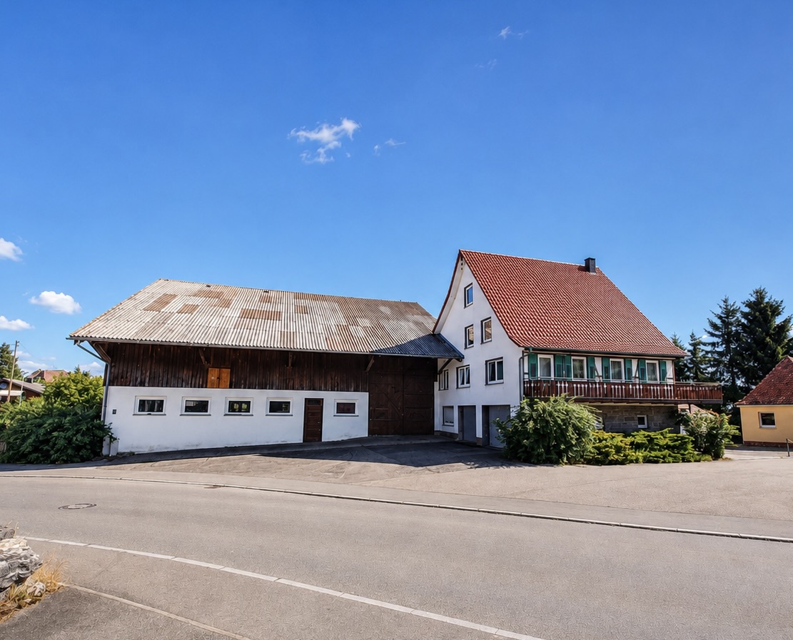 A white farmhouse with a red roof attached to a large wooden barn under a clear blue sky on a sunny day. [AI-generated text]