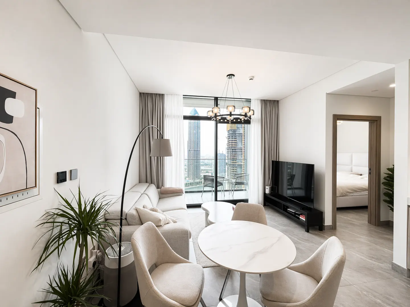 A modern apartment living room with a white sofa, round table, and city view through a large window.