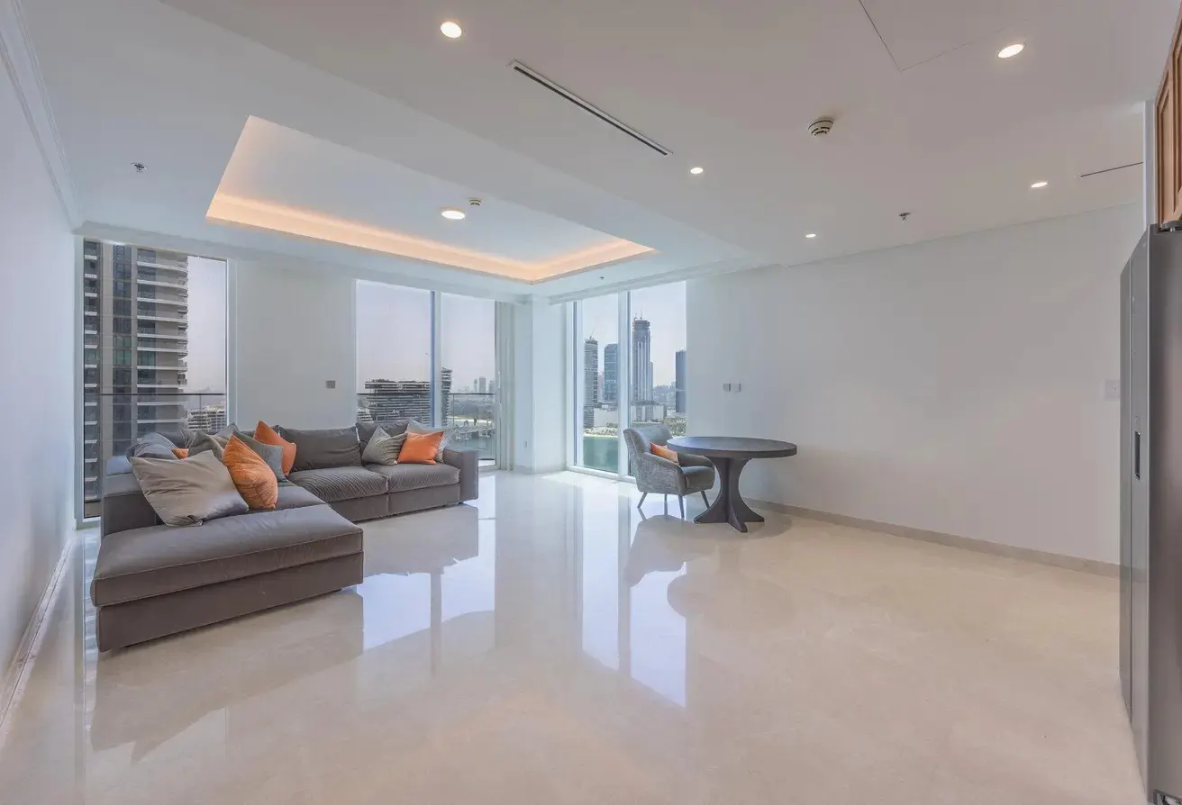 Bright, modern living room with a gray sectional sofa, orange pillows, round table, and city views through large windows.
