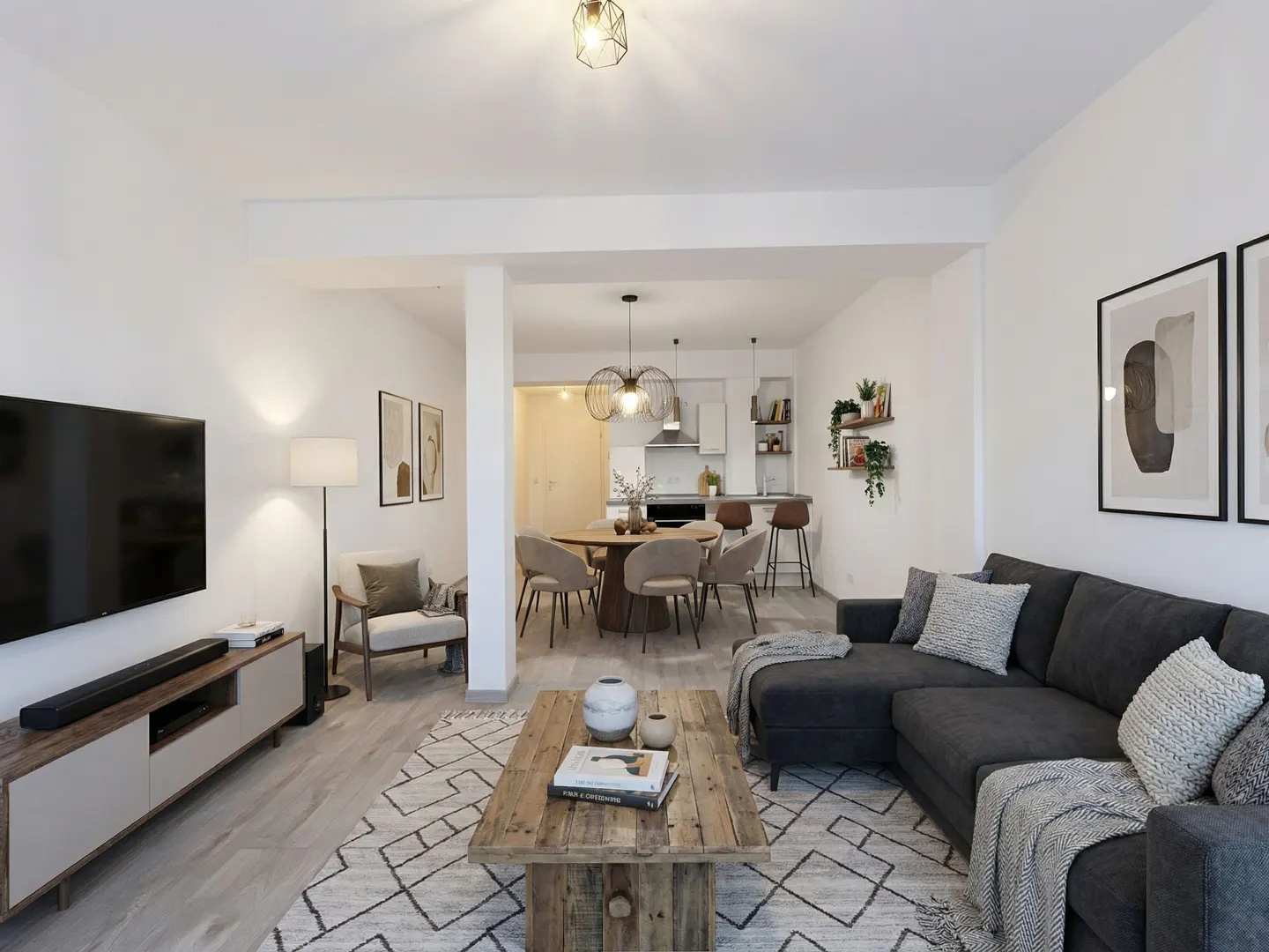Open-concept living space with a gray sectional sofa, wood coffee table, dining area, and kitchen in the background.