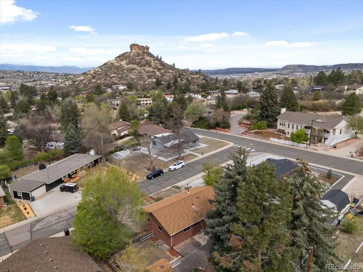 Aerial view of a residential neighborhood with houses, trees, and a large rock formation in the background under a blue sky.