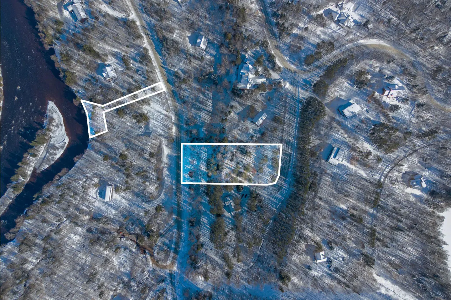 Aerial view of snow-covered land with a river, trees, and houses. Two plots of land are outlined in white.