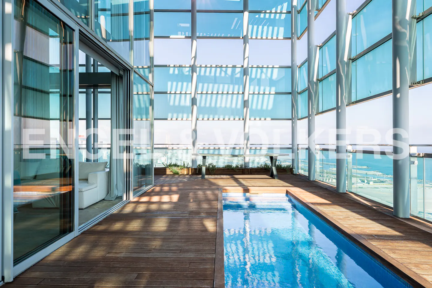 Modern penthouse with a pool on a wooden deck, surrounded by glass walls and a view of the ocean.