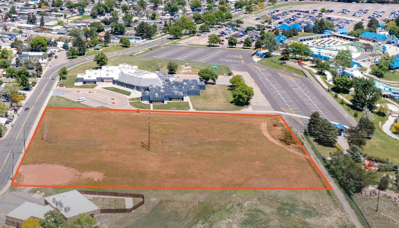 Aerial view of a large, vacant rectangular lot outlined in red, situated near a parking lot and commercial buildings.