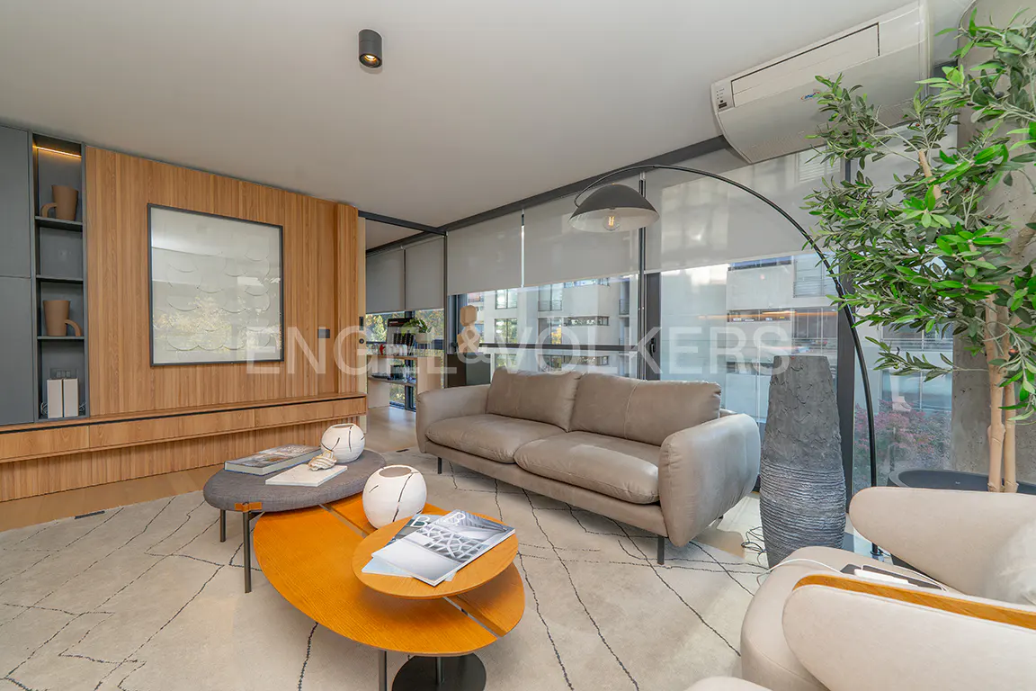Living room with a gray sofa, two coffee tables, and a large window with a tree in front.
